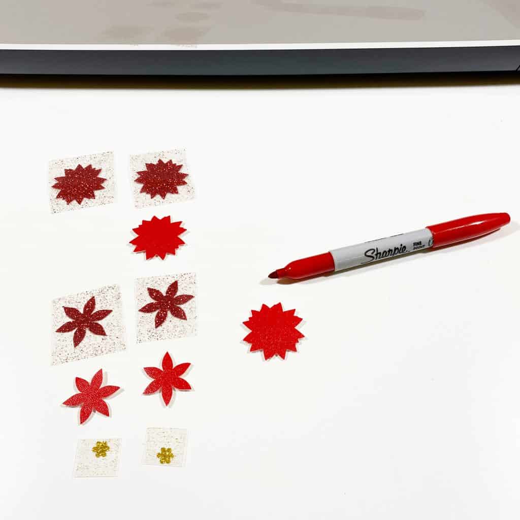 A red Sharpie alongside cut red faux leather poinsettia shapes. 