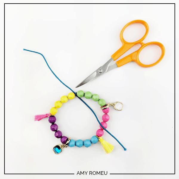 making a knot in the cord of stretchy stack bracelet with beads, charms and tassels